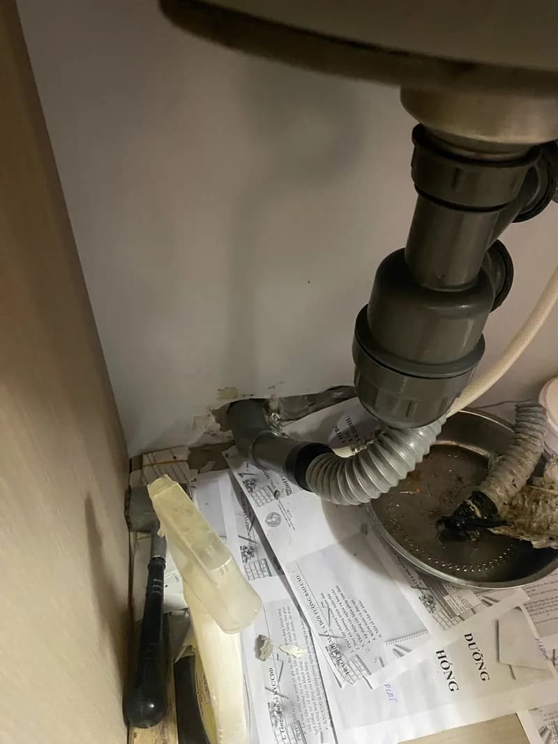 Mở tủ bếp ra thấy cái ống thoát lavabo bị hở, nước rỉ ra ướt hết ván tại Quận 11